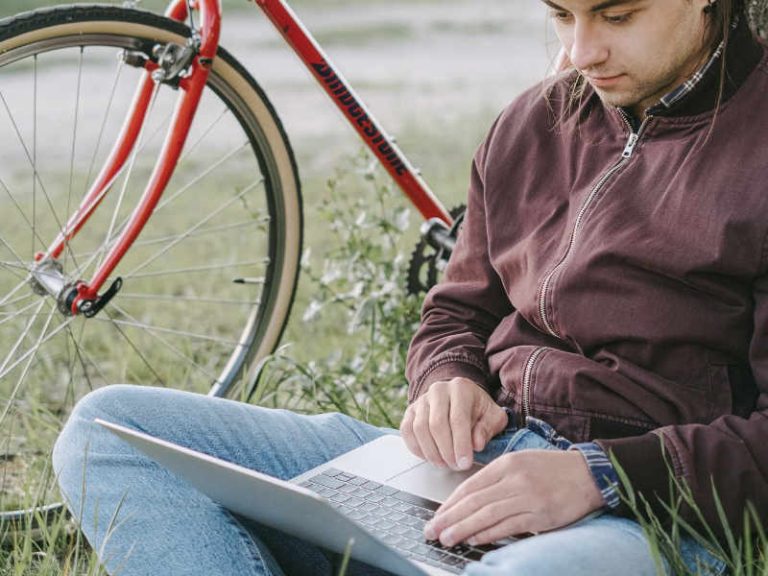 A man leans against his tree by his bike using a computer to respond to the budget consultation