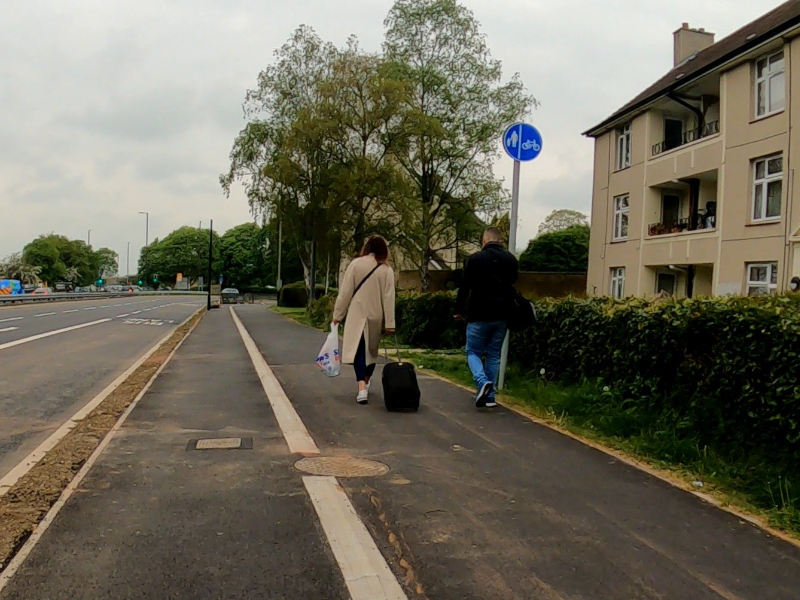 Two pedestrians keep away from traffic by walking in the Gloucestershire cycle way below a sign showing the arrangement of users