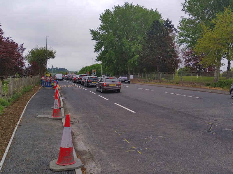 A photo of the approach from Bishop's Cleeve to the southam lane racecourse junction with stationary vehicles and three approach lanes.