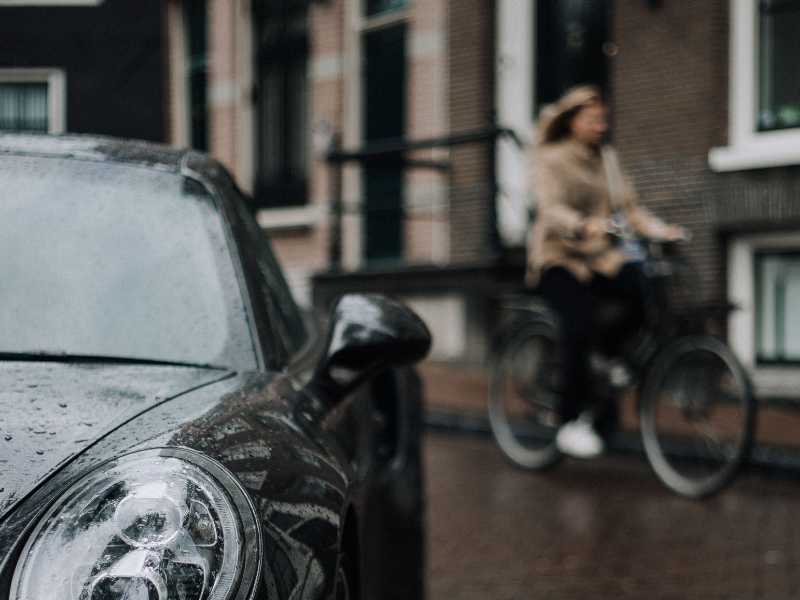 A woman cycling alongside a car, highlighting the range of street users who the Gloucestershire Road Safety policy needs to protect.